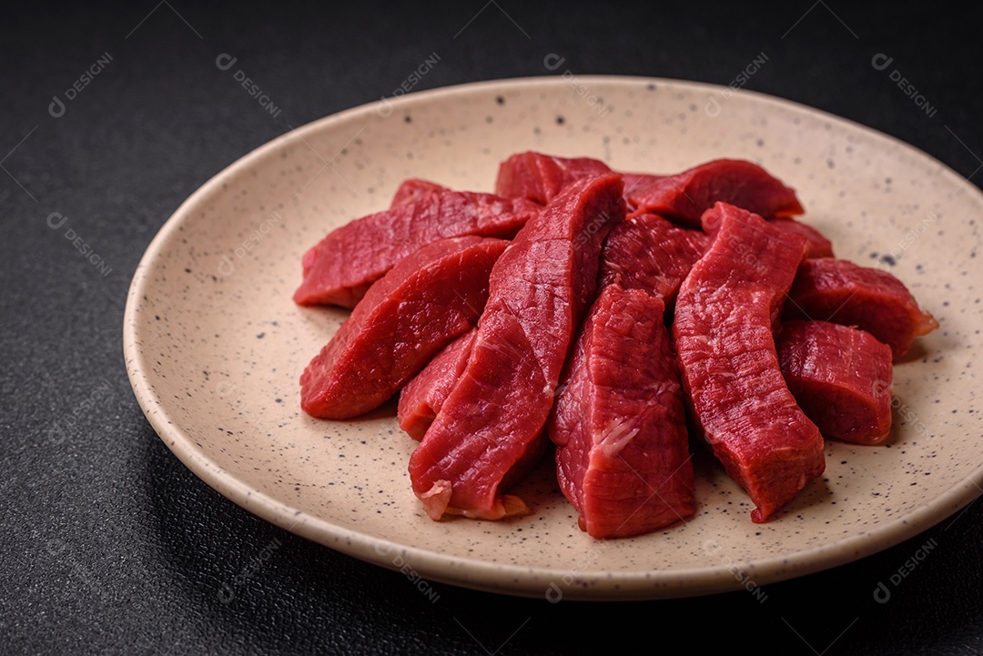 Carne crua fresca e suculenta com sal, especiarias e ervas sobre um fundo de concreto texturizado escuro