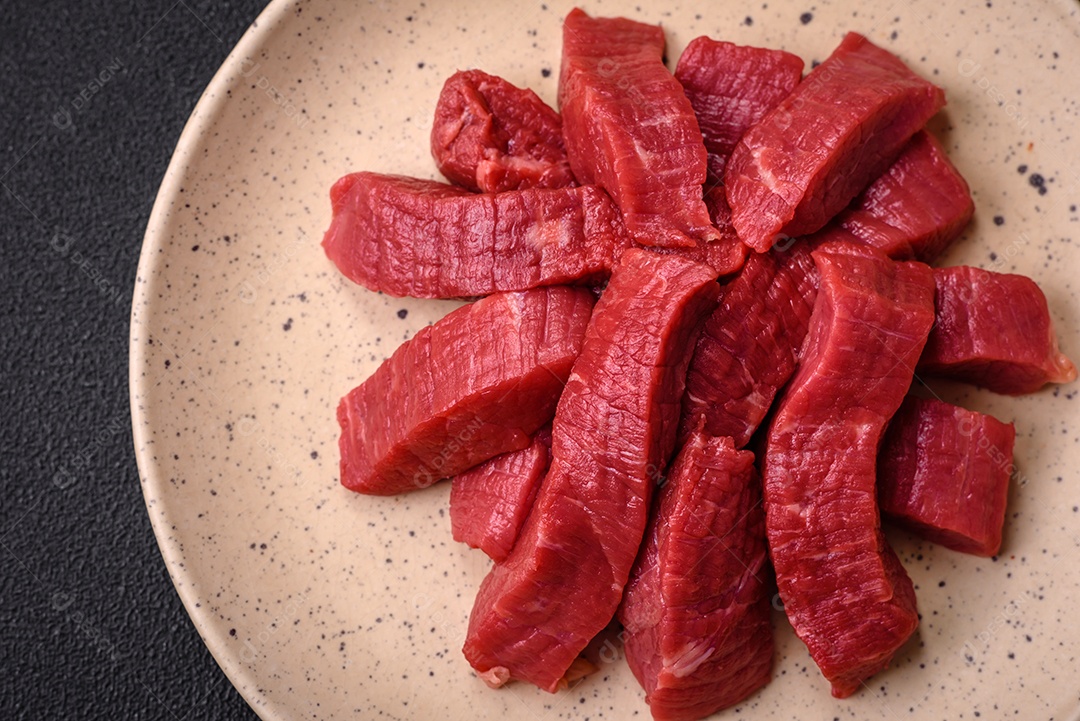 Carne crua fresca e suculenta com sal, especiarias e ervas sobre um fundo de concreto texturizado escuro