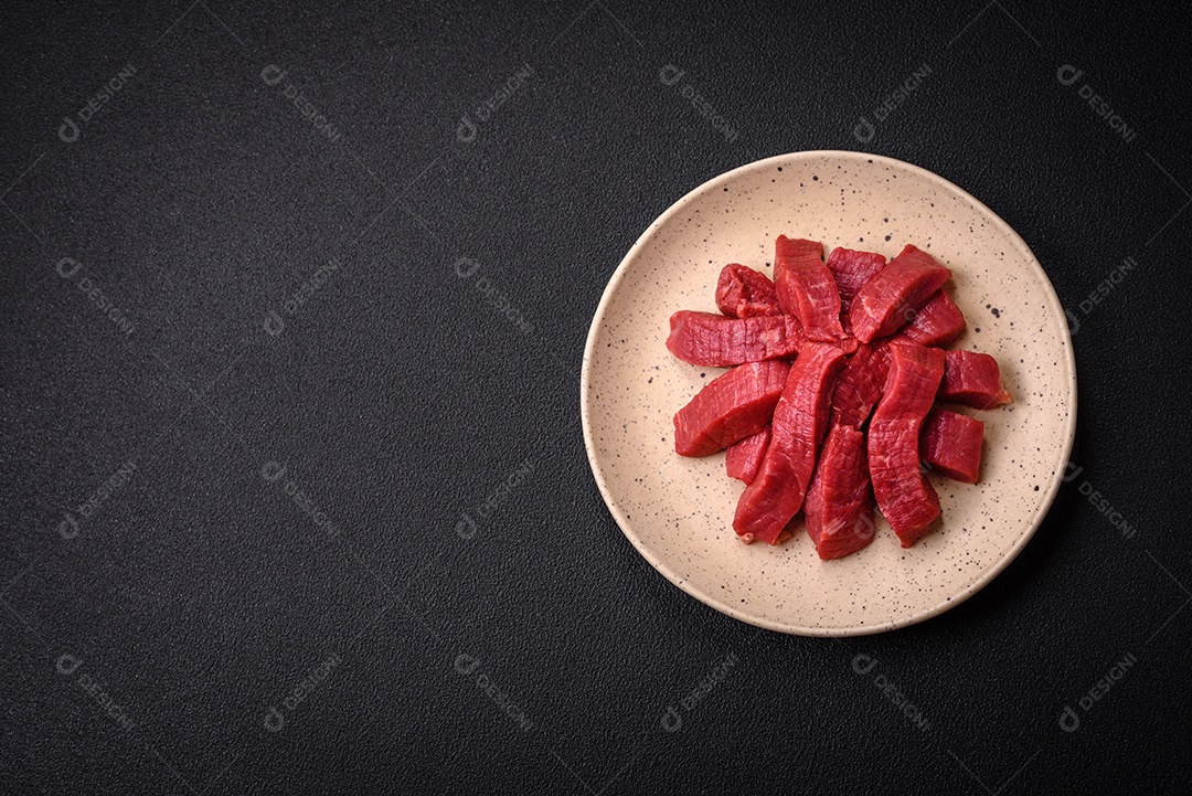 Carne crua fresca e suculenta com sal, especiarias e ervas sobre um fundo de concreto texturizado escuro