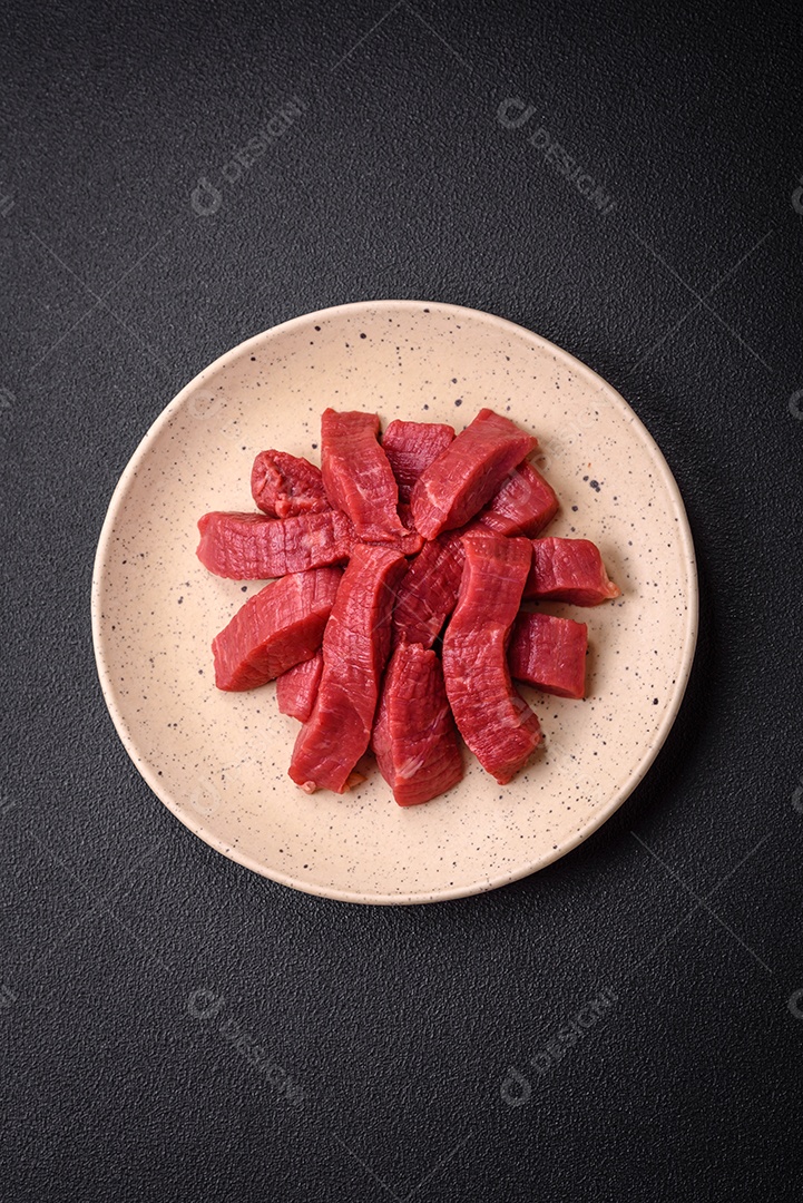 Carne crua fresca e suculenta com sal, especiarias e ervas sobre um fundo de concreto texturizado escuro