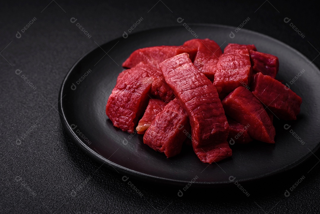 Carne crua fresca e suculenta com sal, especiarias e ervas sobre um fundo de concreto texturizado escuro