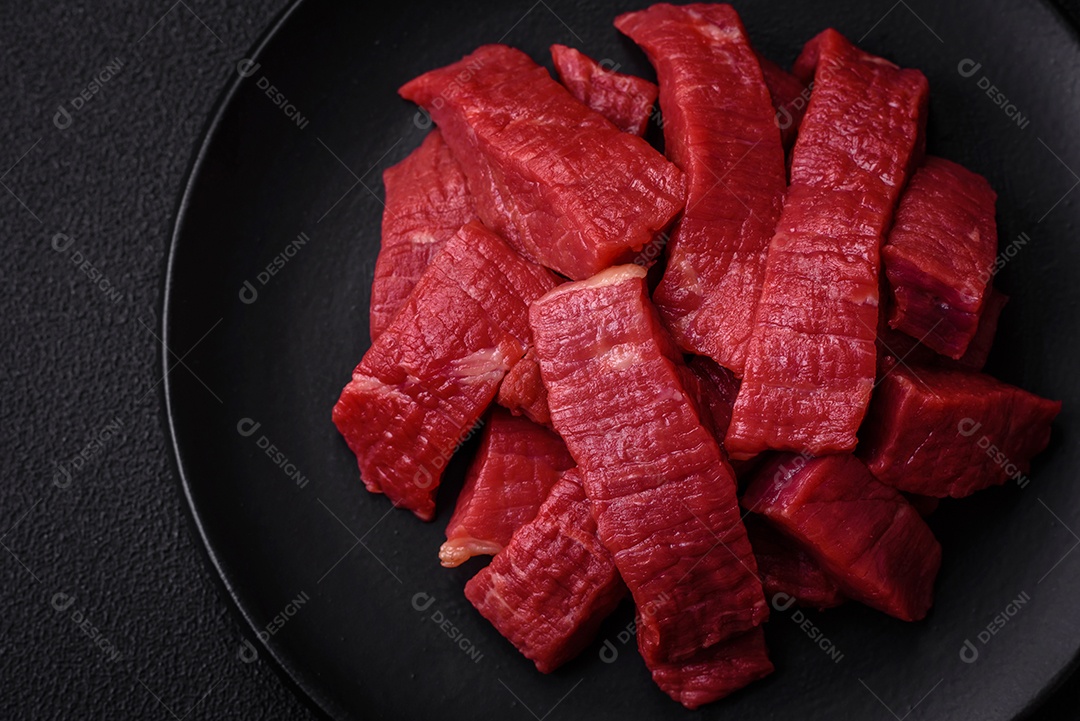 Carne crua fresca e suculenta com sal, especiarias e ervas sobre um fundo de concreto texturizado escuro