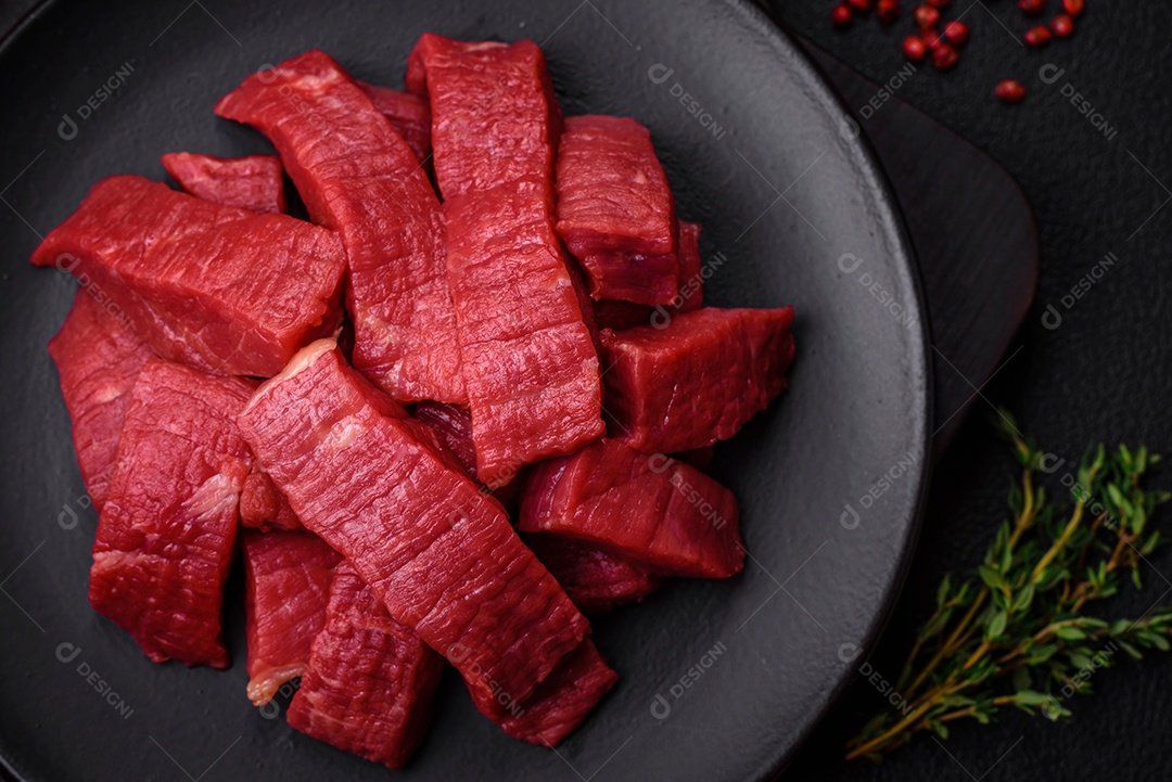 Carne crua fresca e suculenta com sal, especiarias e ervas sobre um fundo de concreto texturizado escuro