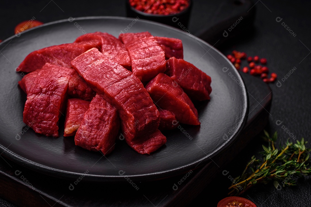 Carne crua fresca e suculenta com sal, especiarias e ervas sobre um fundo de concreto texturizado escuro