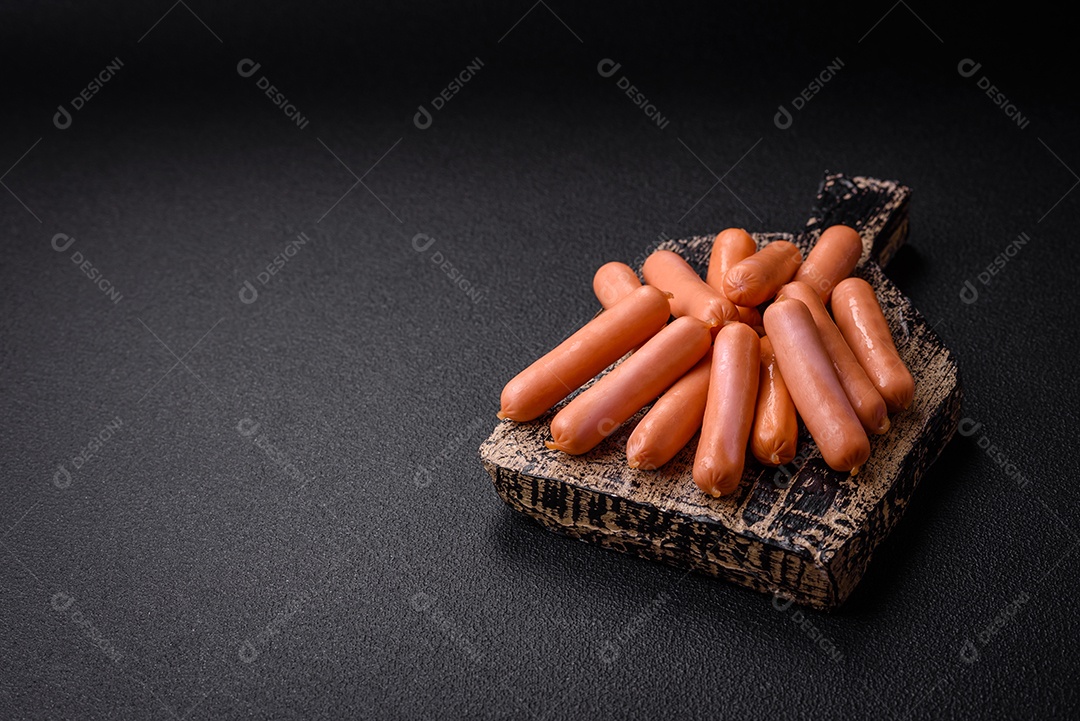 Deliciosas salsichas pequenas com sal, especiarias e ervas sobre um fundo escuro de concreto