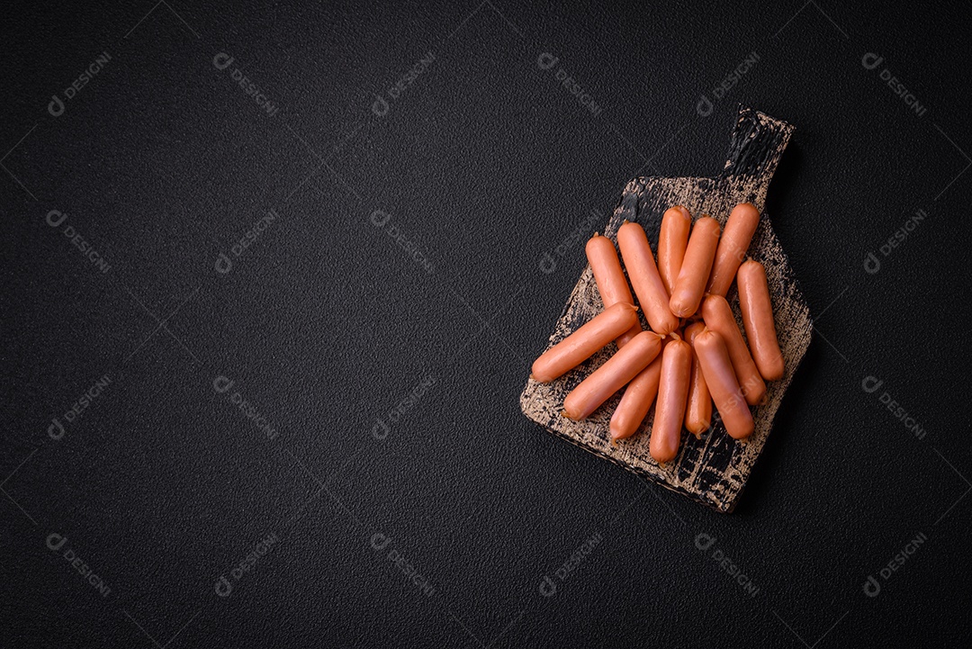 Deliciosas salsichas pequenas com sal, especiarias e ervas sobre um fundo escuro de concreto