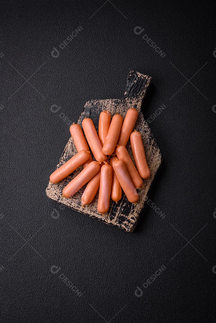 Deliciosas salsichas pequenas com sal, especiarias e ervas sobre um fundo escuro de concreto