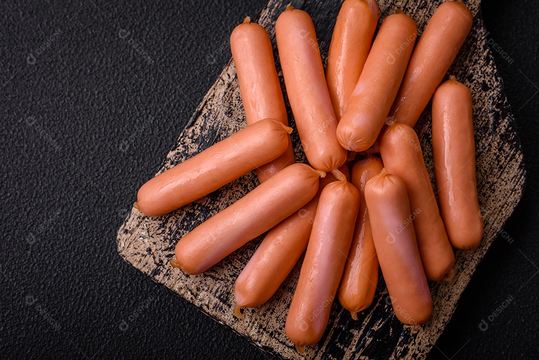 Deliciosas salsichas pequenas com sal, especiarias e ervas sobre um fundo escuro de concreto