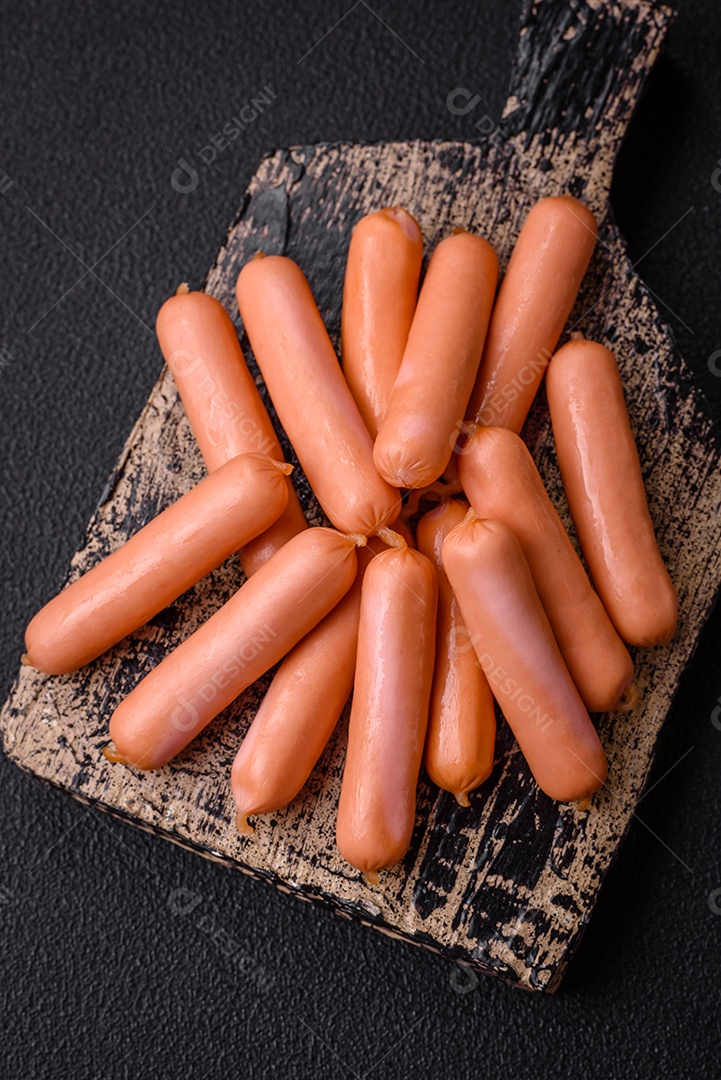 Deliciosas salsichas pequenas com sal, especiarias e ervas sobre um fundo escuro de concreto