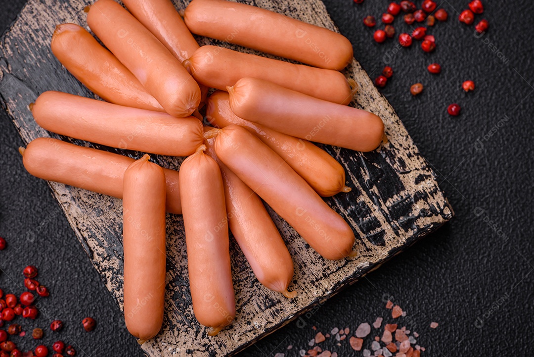 Deliciosas salsichas pequenas com sal, especiarias e ervas sobre um fundo escuro de concreto