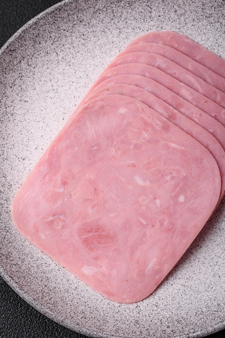 Delicioso presunto fresco cortado em fatias com sal, especiarias e ervas sobre um fundo escuro de concreto