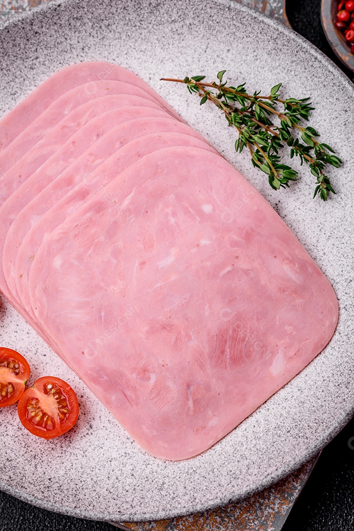 Delicioso presunto fresco cortado em fatias com sal, especiarias e ervas sobre um fundo escuro de concreto