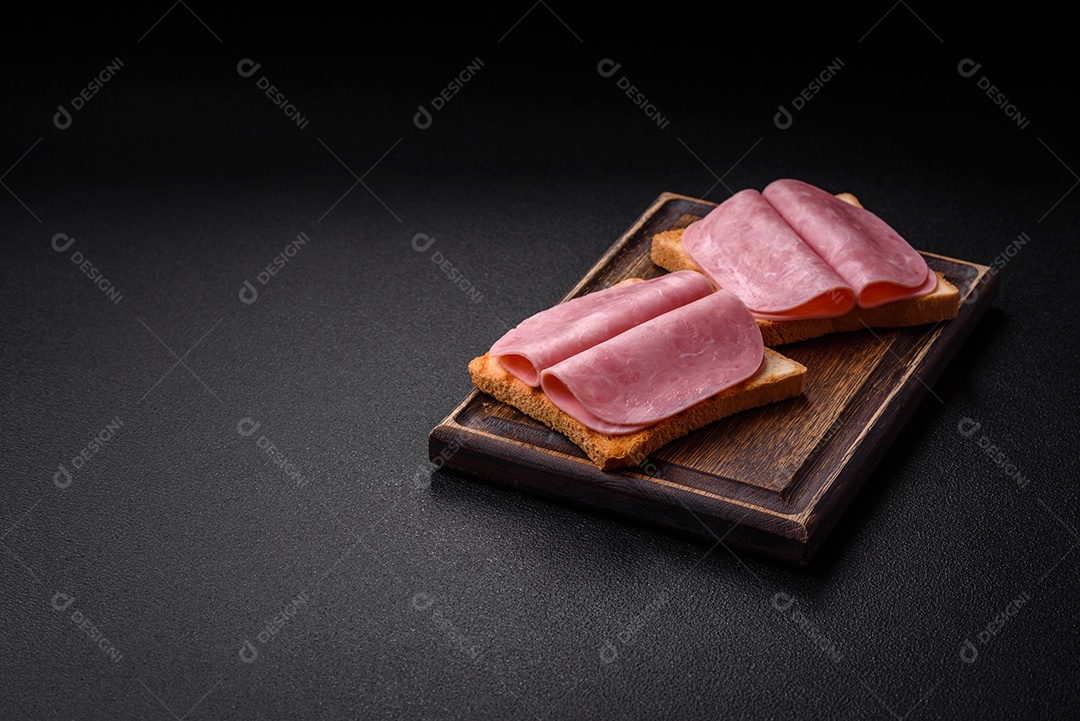 Delicioso sanduíche com pão torrado, presunto, tomate, sal e especiarias sobre um fundo escuro de concreto