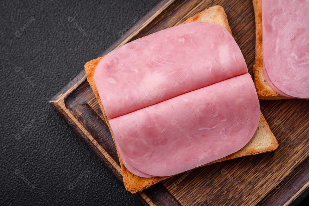 Delicioso sanduíche com pão torrado, presunto, tomate, sal e especiarias sobre um fundo escuro de concreto