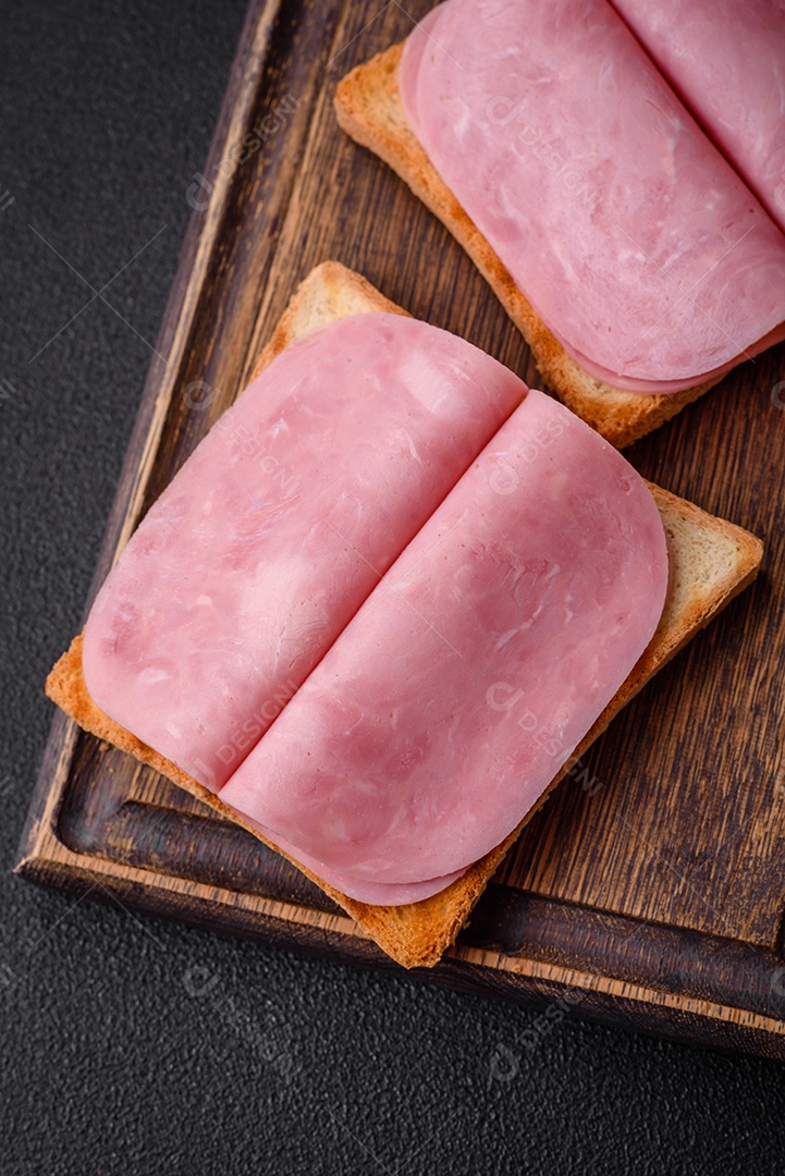 Delicioso sanduíche com pão torrado, presunto, tomate, sal e especiarias sobre um fundo escuro de concreto