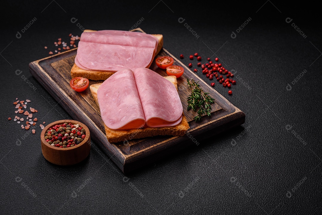 Delicioso sanduíche com pão torrado, presunto, tomate, sal e especiarias sobre um fundo escuro de concreto