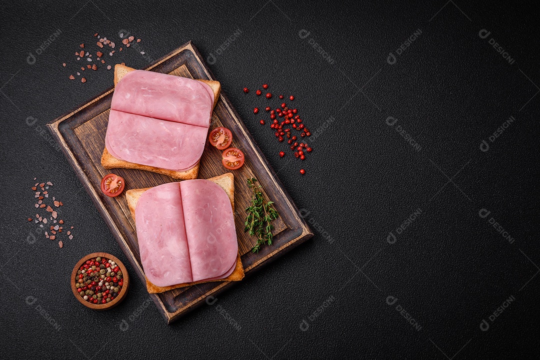 Delicioso sanduíche com pão torrado, presunto, tomate, sal e especiarias sobre um fundo escuro de concreto