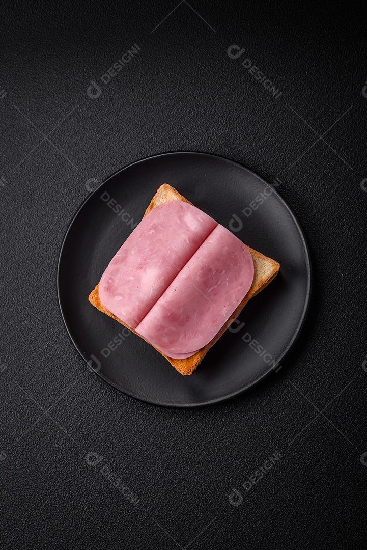 Delicioso sanduíche com pão torrado, presunto, tomate, sal e especiarias sobre um fundo escuro de concreto