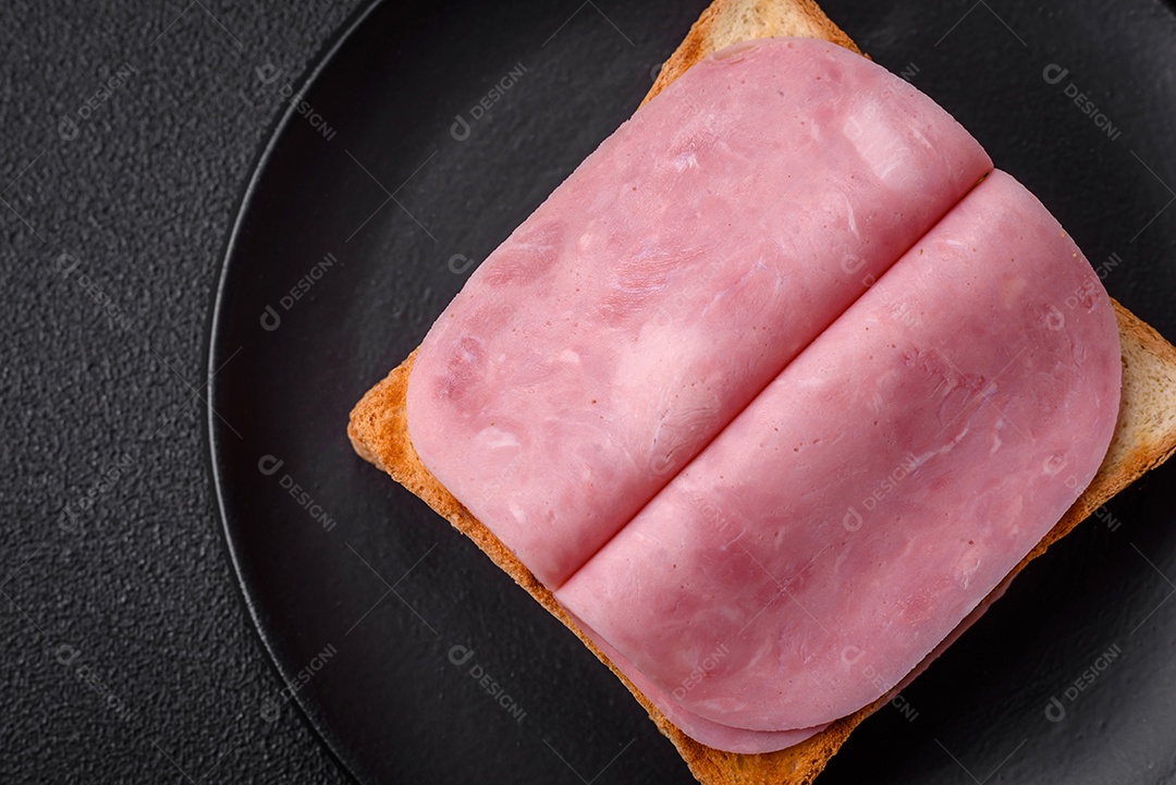 Delicioso sanduíche com pão torrado, presunto, tomate, sal e especiarias sobre um fundo escuro de concreto