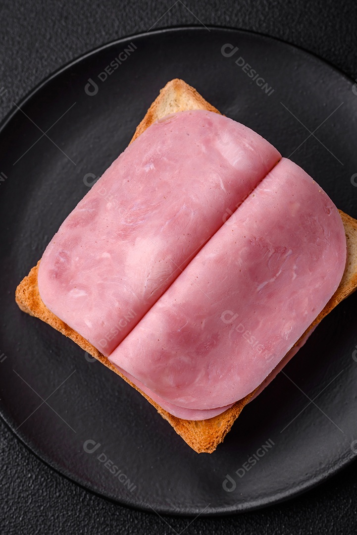 Delicioso sanduíche com pão torrado, presunto, tomate, sal e especiarias sobre um fundo escuro de concreto