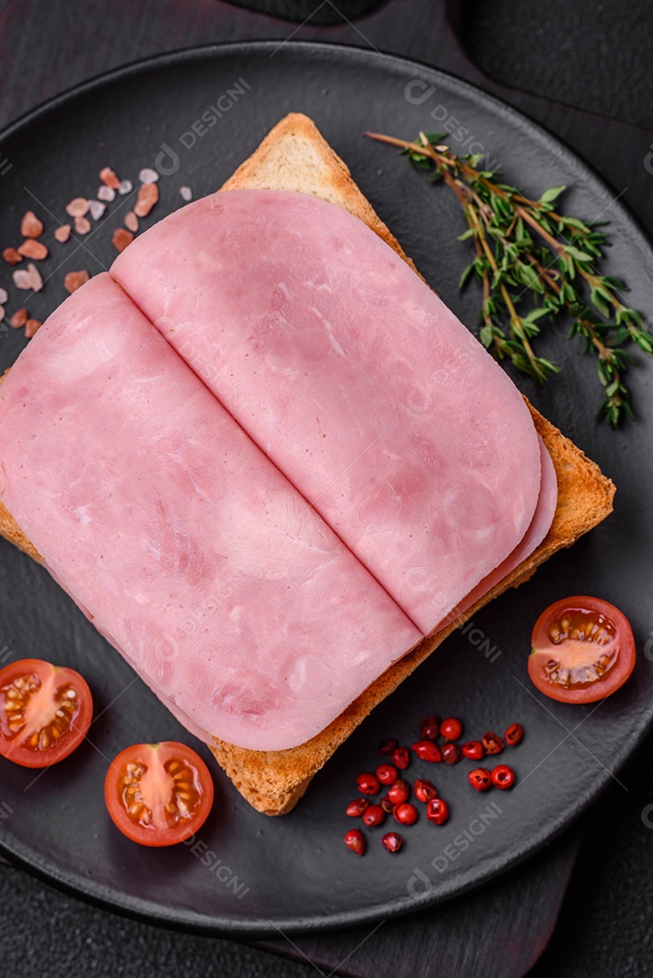 Delicioso sanduíche com pão torrado, presunto, tomate, sal e especiarias sobre um fundo escuro de concreto