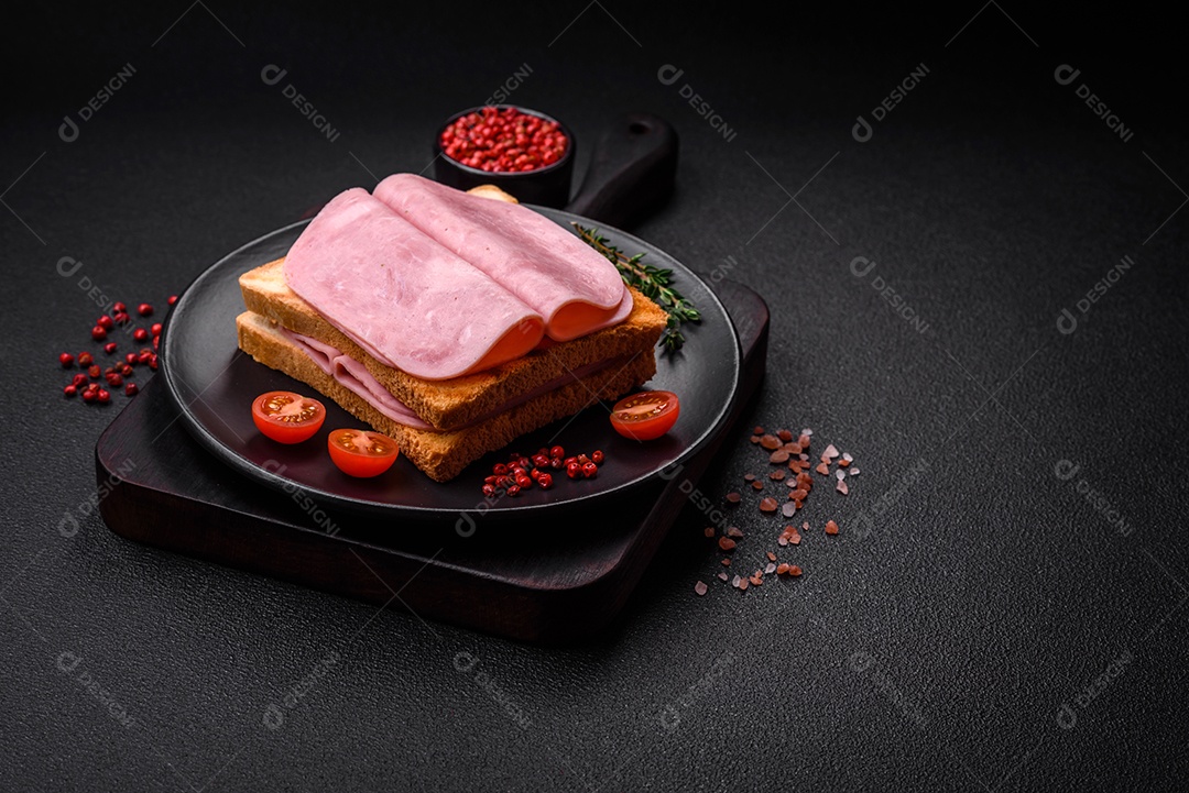 Delicioso sanduíche com pão torrado, presunto, tomate, sal e especiarias sobre um fundo escuro de concreto
