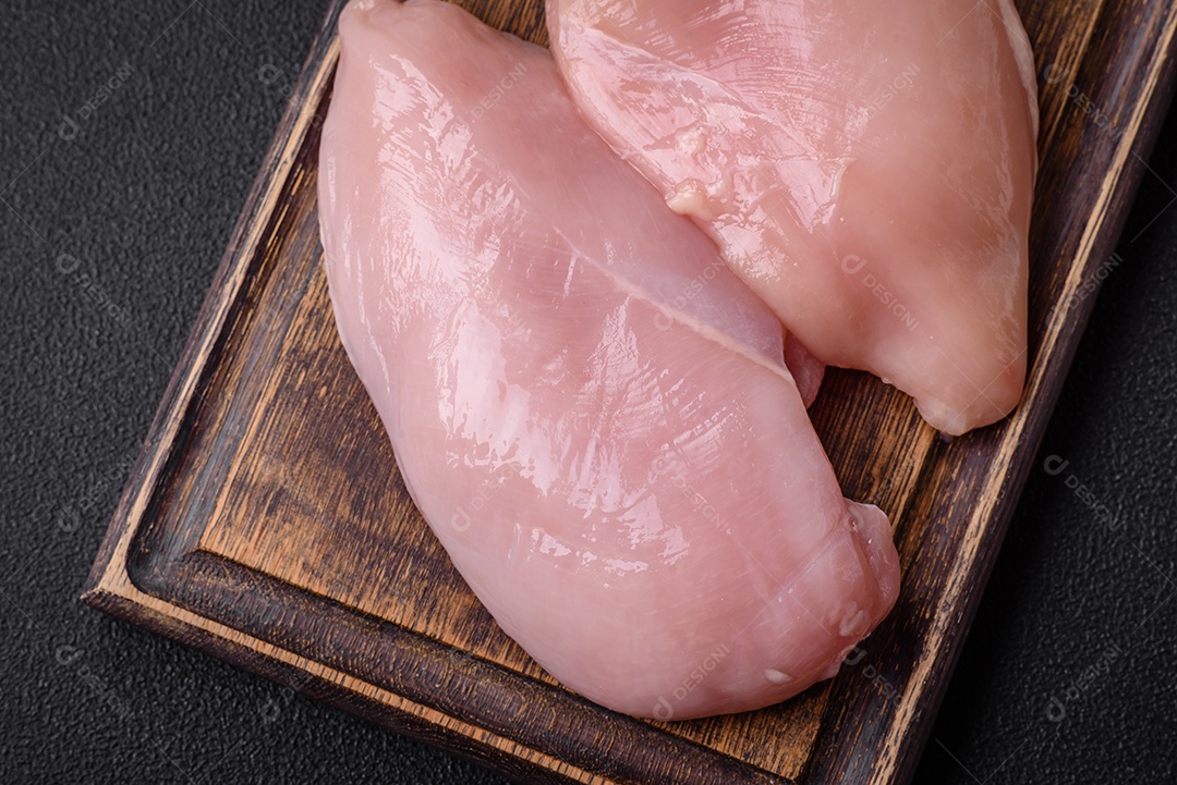 Filé de frango fresco sobre uma mesa de concreto escuro com especiarias e ervas. Preparação para cozinhar pratos de carne