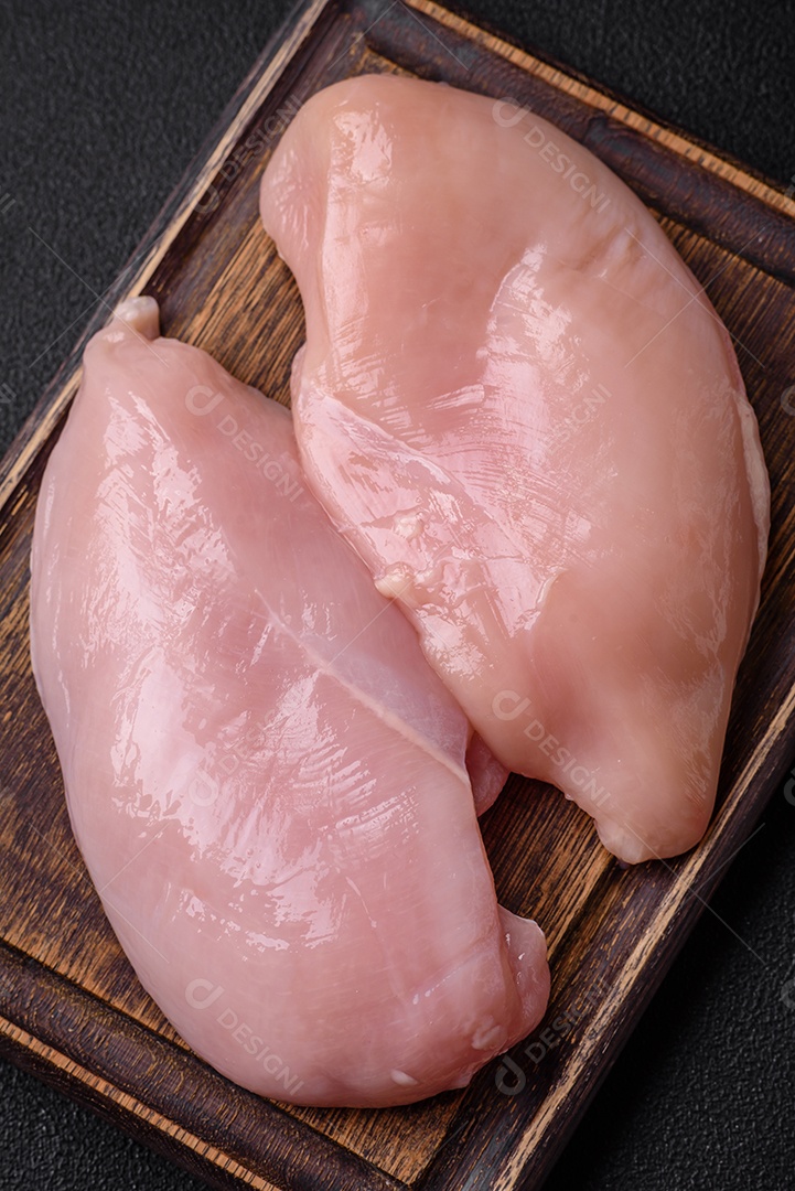 Filé de frango fresco sobre uma mesa de concreto escuro com especiarias e ervas. Preparação para cozinhar pratos de carne