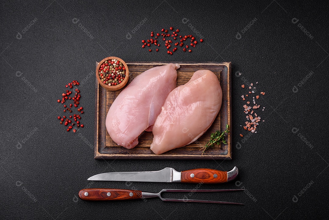 Filé de frango fresco sobre uma mesa de concreto escuro com especiarias e ervas. Preparação para cozinhar pratos de carne