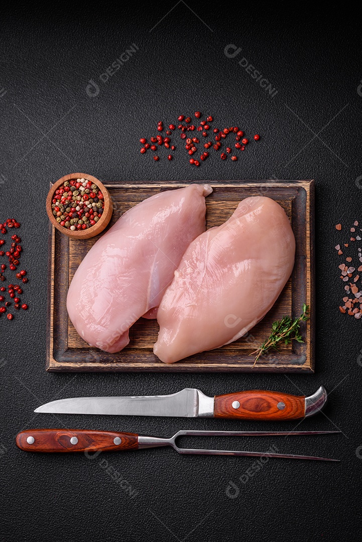 Filé de frango fresco sobre uma mesa de concreto escuro com especiarias e ervas. Preparação para cozinhar pratos de carne