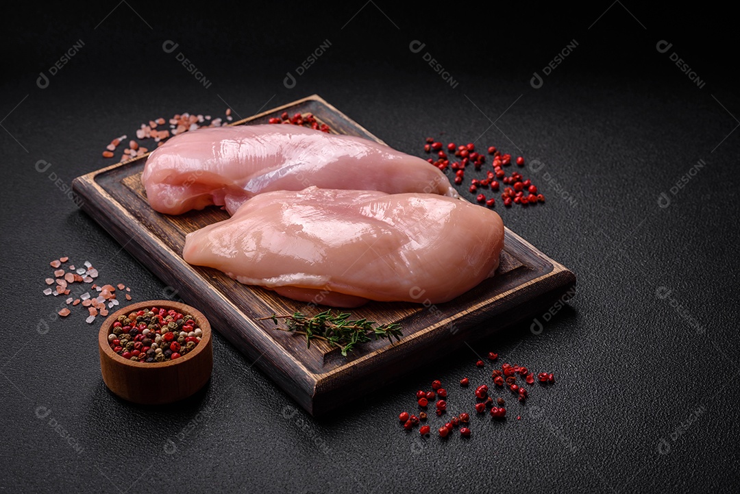 Filé de frango fresco sobre uma mesa de concreto escuro com especiarias e ervas. Preparação para cozinhar pratos de carne