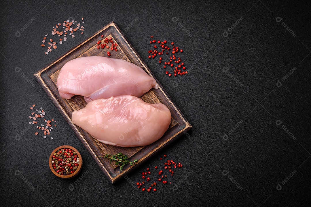 Filé de frango fresco sobre uma mesa de concreto escuro com especiarias e ervas. Preparação para cozinhar pratos de carne