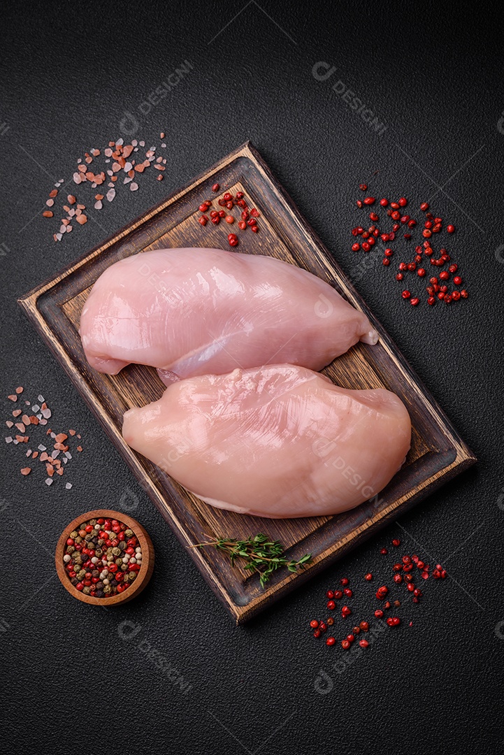 Filé de frango fresco sobre uma mesa de concreto escuro com especiarias e ervas. Preparação para cozinhar pratos de carne