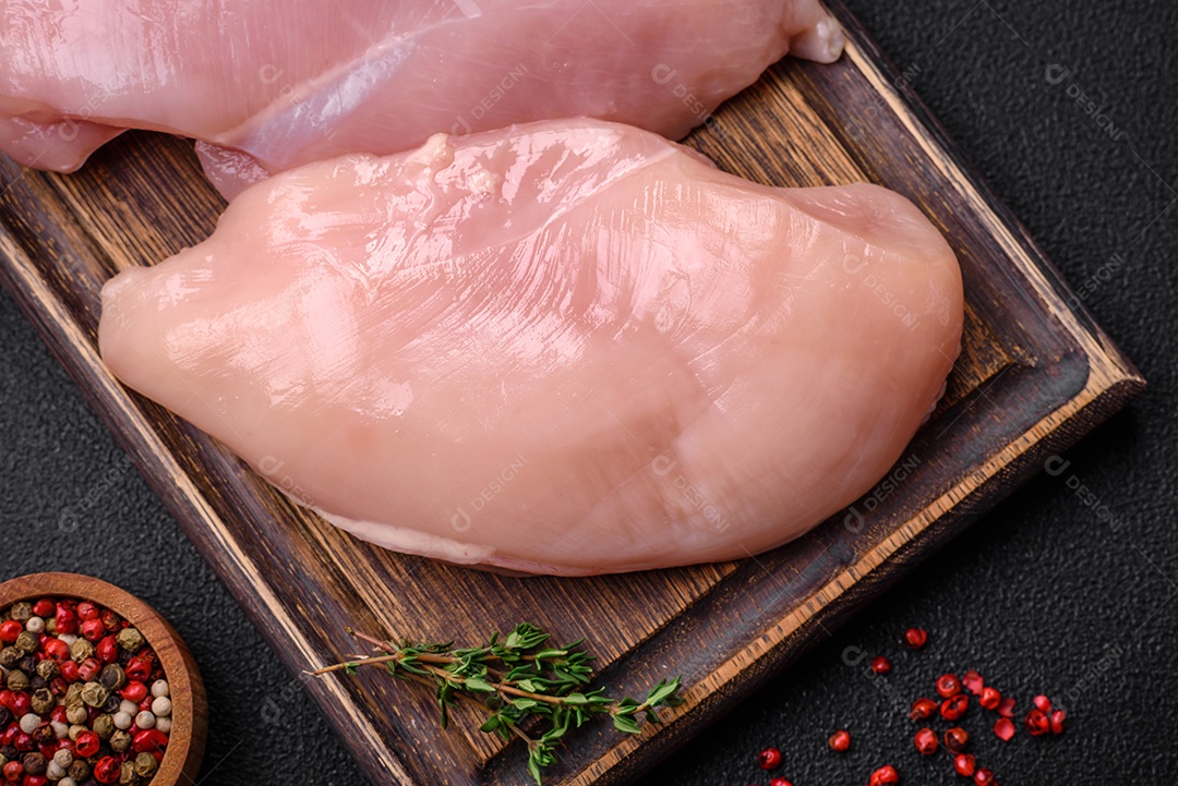 Filé de frango fresco sobre uma mesa de concreto escuro com especiarias e ervas. Preparação para cozinhar pratos de carne