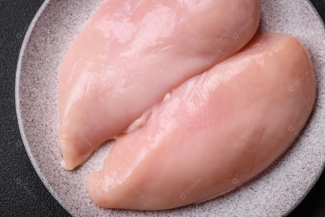 Filé de frango fresco sobre uma mesa de concreto escuro com especiarias e ervas. Preparação para cozinhar pratos de carne