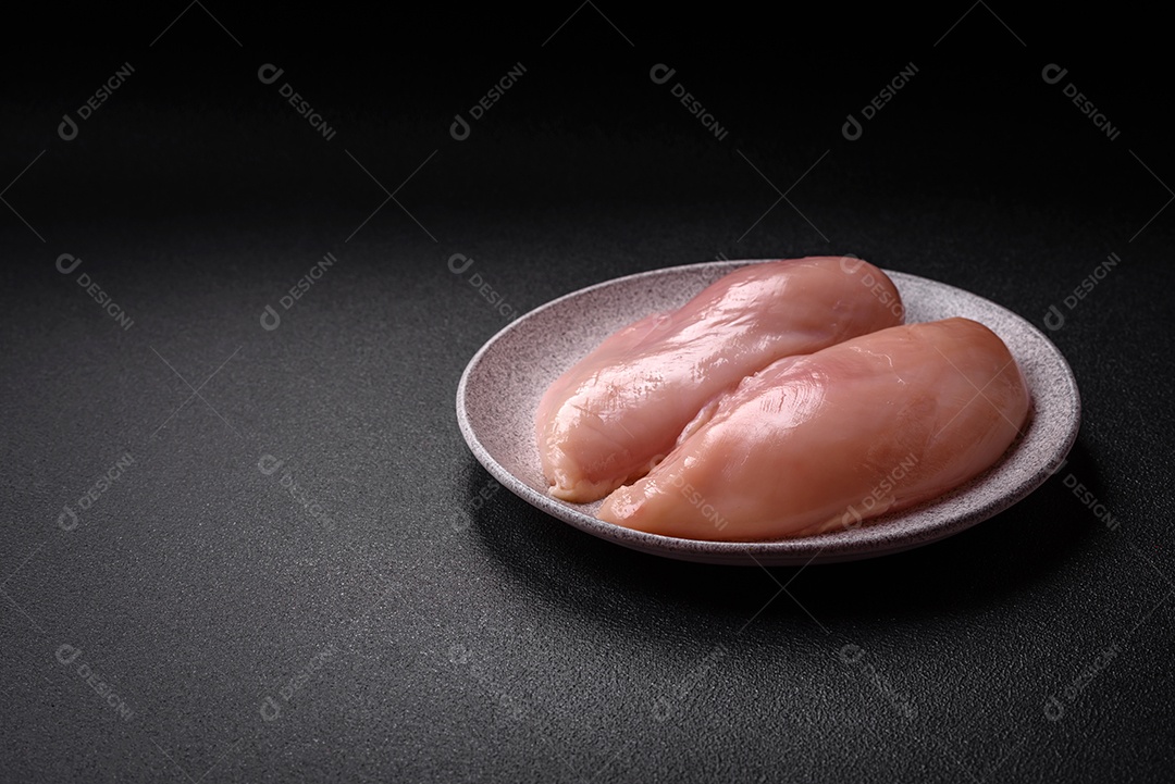 Filé de frango fresco sobre uma mesa de concreto escuro com especiarias e ervas. Preparação para cozinhar pratos de carne