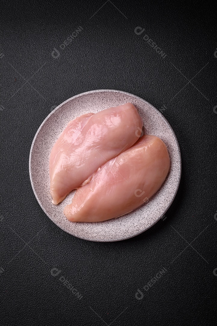 Filé de frango fresco sobre uma mesa de concreto escuro com especiarias e ervas. Preparação para cozinhar pratos de carne