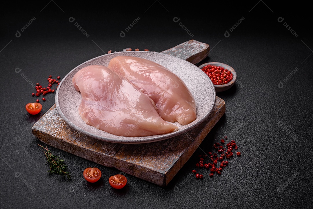 Filé de frango fresco sobre uma mesa de concreto escuro com especiarias e ervas. Preparação para cozinhar pratos de carne