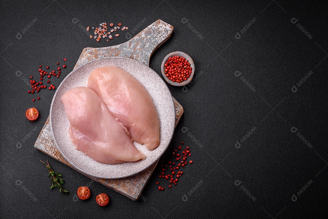 Filé de frango fresco sobre uma mesa de concreto escuro com especiarias e ervas. Preparação para cozinhar pratos de carne