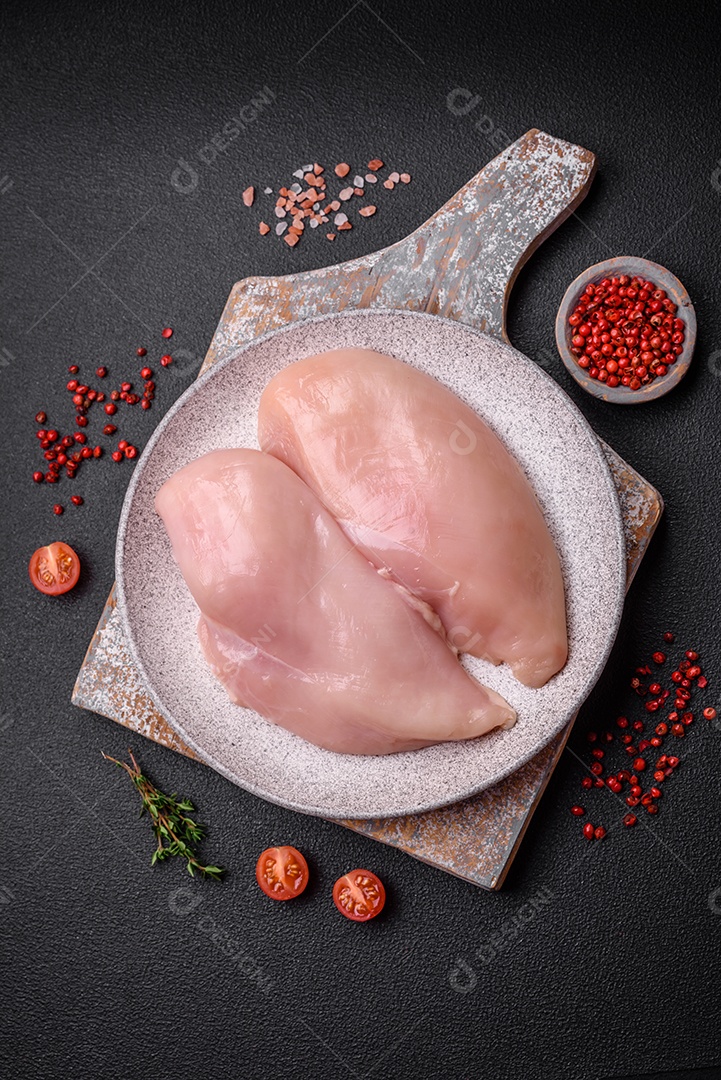 Filé de frango fresco sobre uma mesa de concreto escuro com especiarias e ervas. Preparação para cozinhar pratos de carne