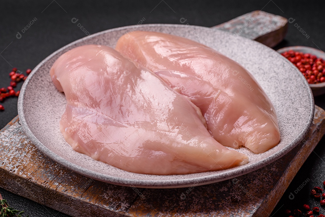 Filé de frango fresco sobre uma mesa de concreto escuro com especiarias e ervas. Preparação para cozinhar pratos de carne