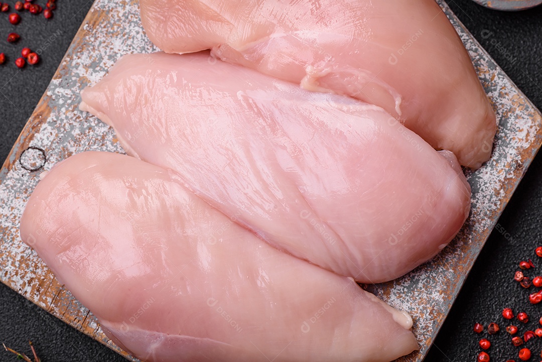 Filé de frango fresco sobre uma mesa de concreto escuro com especiarias e ervas. Preparação para cozinhar pratos de carne