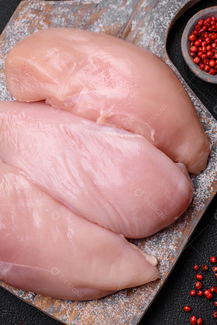 Filé de frango fresco sobre uma mesa de concreto escuro com especiarias e ervas. Preparação para cozinhar pratos de carne