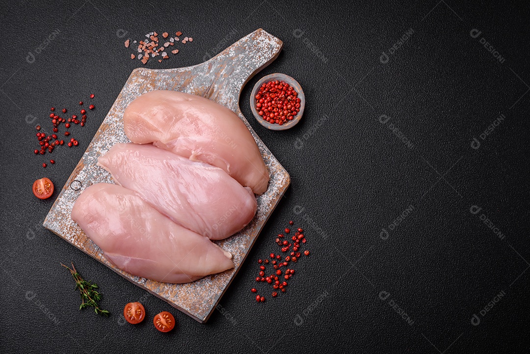 Filé de frango fresco sobre uma mesa de concreto escuro com especiarias e ervas. Preparação para cozinhar pratos de carne