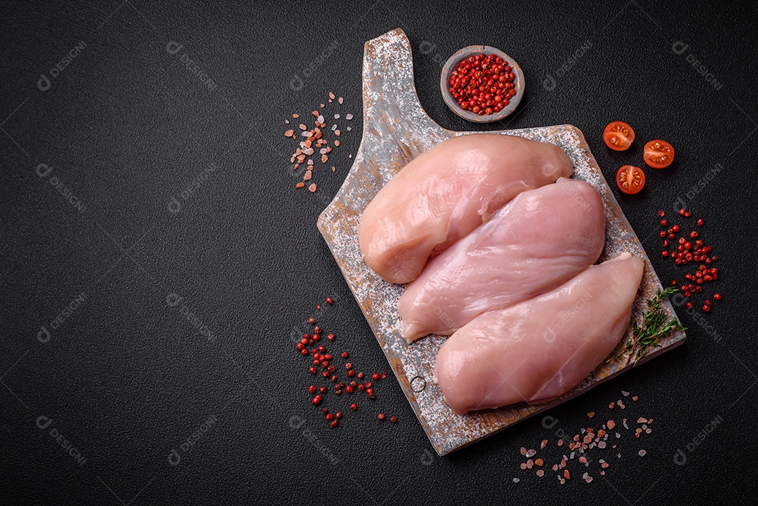 Filé de frango fresco sobre uma mesa de concreto escuro com especiarias e ervas. Preparação para cozinhar pratos de carne