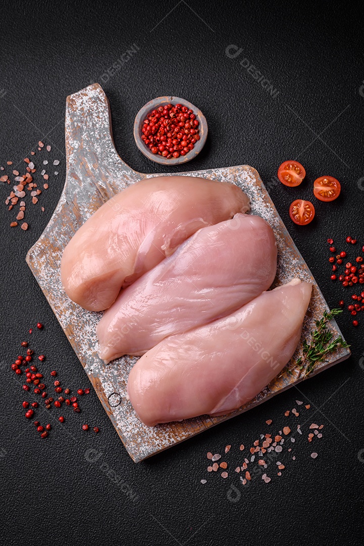 Filé de frango fresco sobre uma mesa de concreto escuro com especiarias e ervas. Preparação para cozinhar pratos de carne