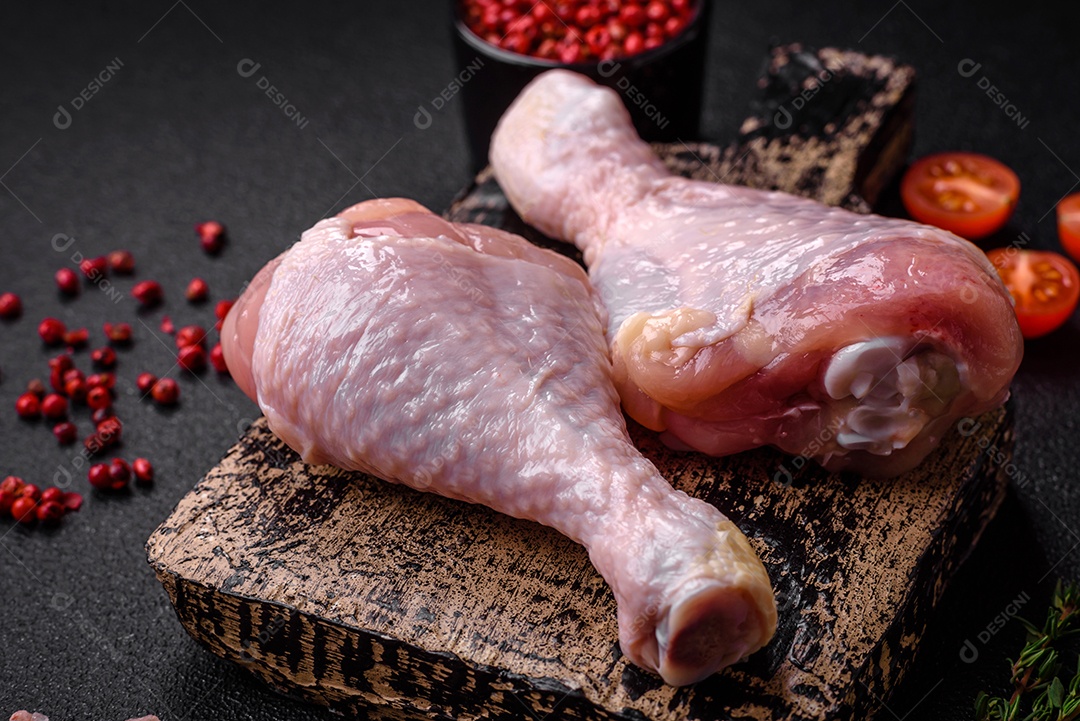 Pernas de frango cru com sal, especiarias e ervas sobre um fundo escuro de concreto. Cozinhando o almoço em casa