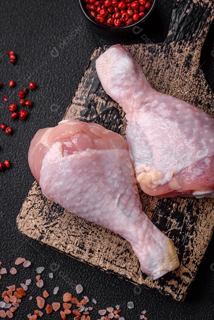 Pernas de frango cru com sal, especiarias e ervas sobre um fundo escuro de concreto. Cozinhando o almoço em casa