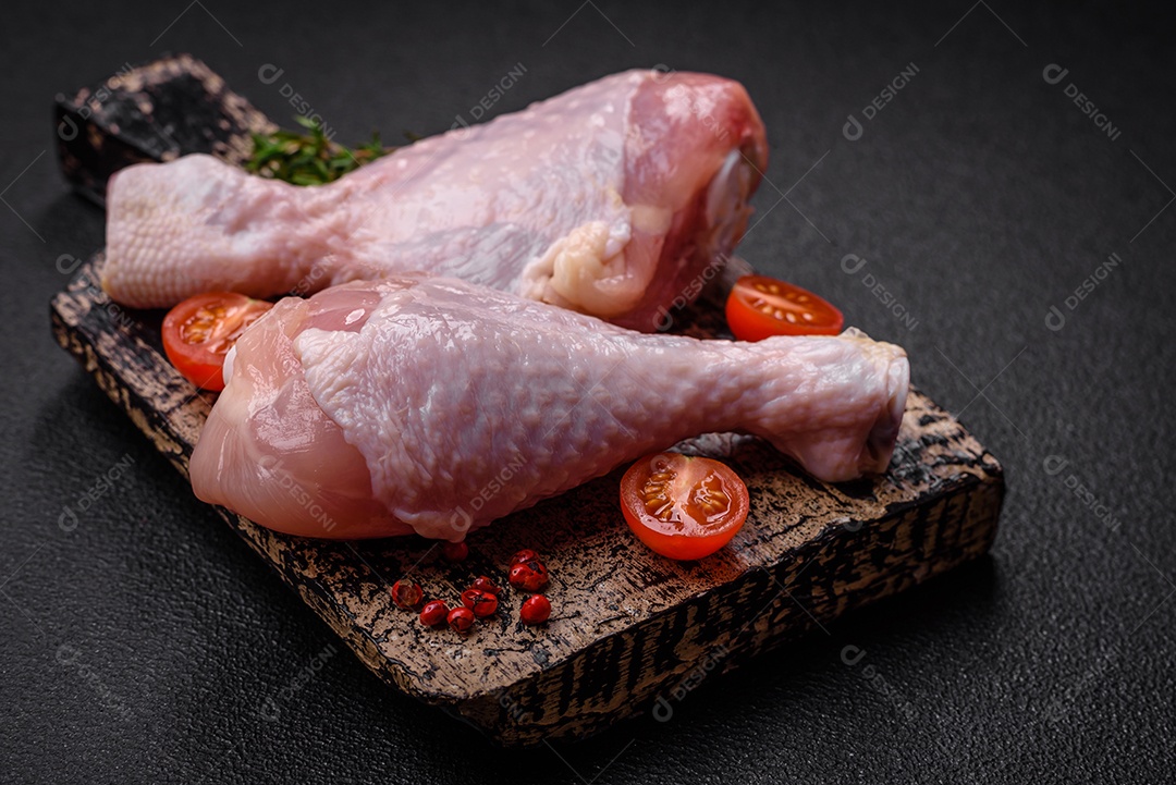 Pernas de frango cru com sal, especiarias e ervas sobre um fundo escuro de concreto. Cozinhando o almoço em casa
