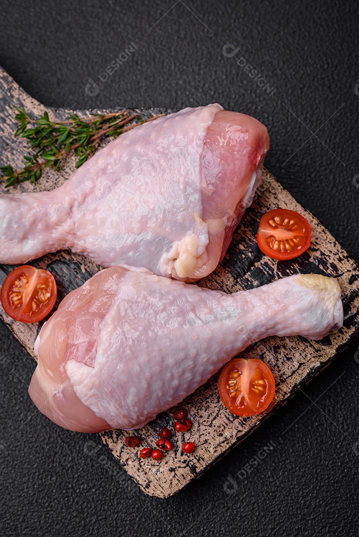 Pernas de frango cru com sal, especiarias e ervas sobre um fundo escuro de concreto. Cozinhando o almoço em casa